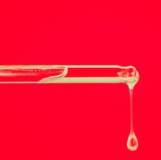 Glass pipette with drop of essential oil on red background. Trendy products of the year. Health and wellness concept. Cosmetic banner with copy space close up of glass pipette with drop of essential oil or face serum on red background trendy products of the year health and wellness concept cosmetic banner with copy space
